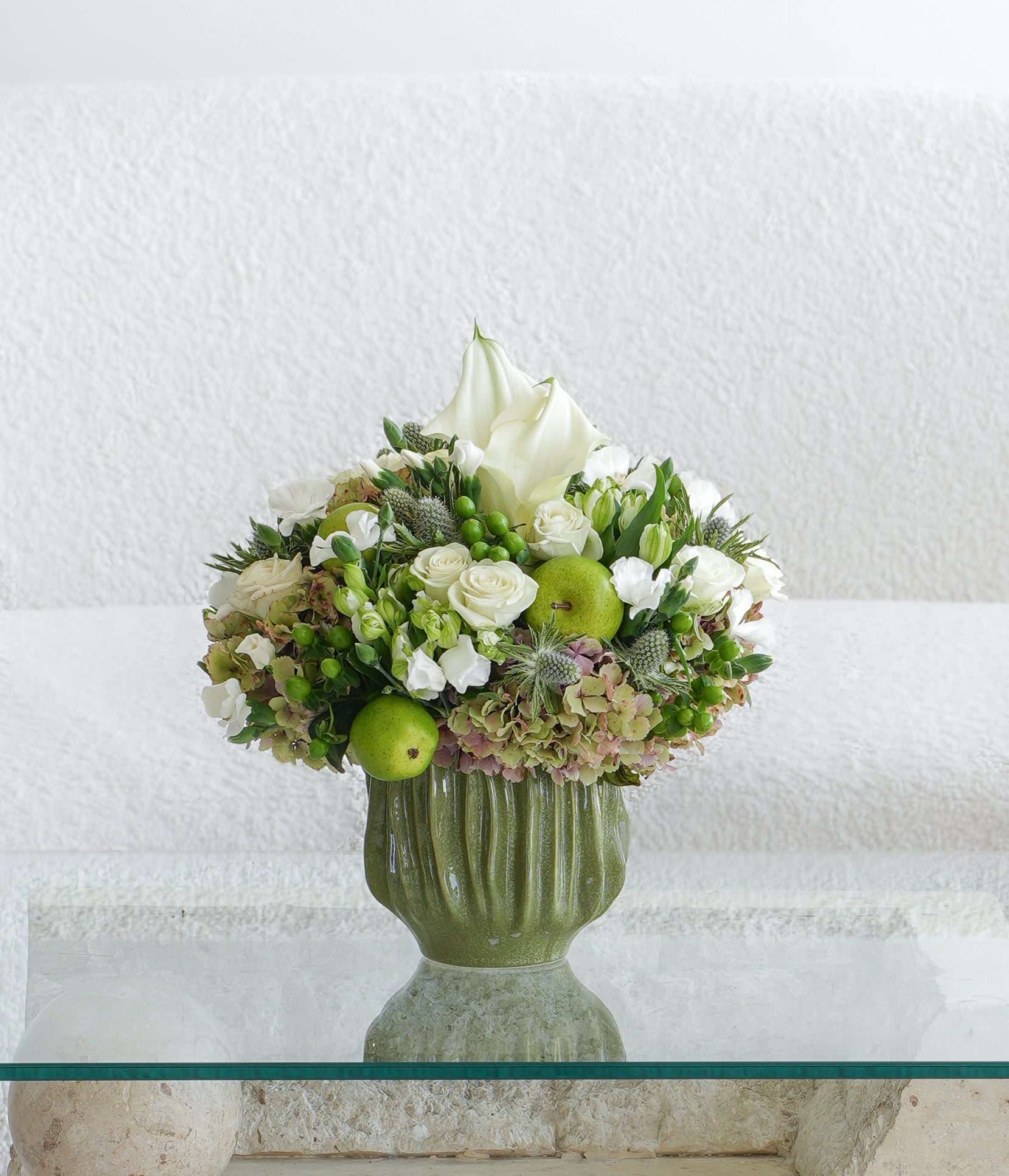 A fresh and refined fall composition of white calla lilies, garden roses, hydrangea, and soft seasonal greens, accented with crisp green apples. Presented in a classic green vessel, this arrangement exudes timeless sophistication—perfect for the home, gifting, or elegant gatherings